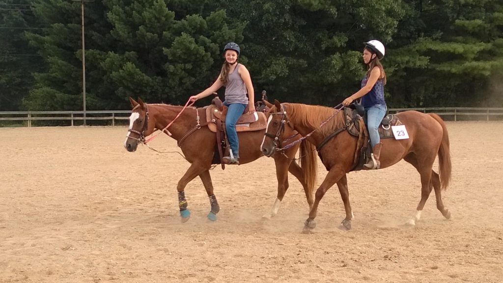 Two teenagers ride horses in a ring.