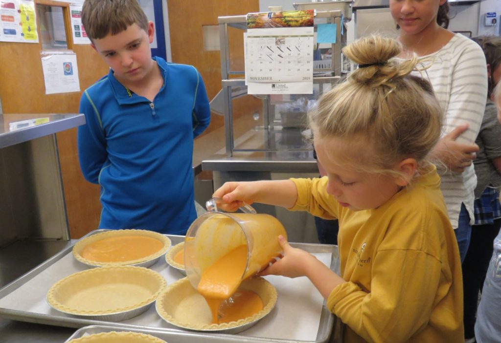 child pouring filling into pies