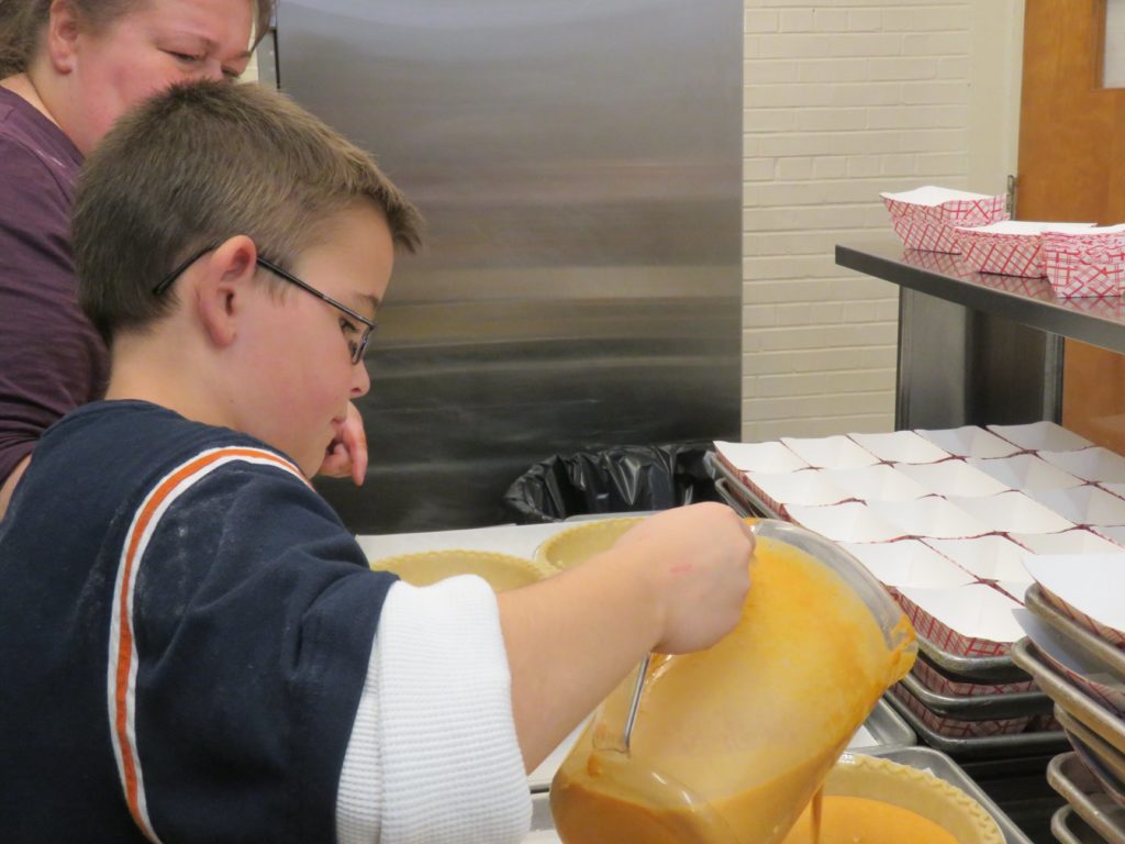 child pouring filling into pies