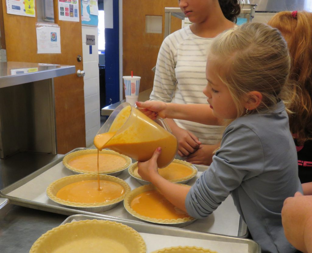 child pouring filling into pies