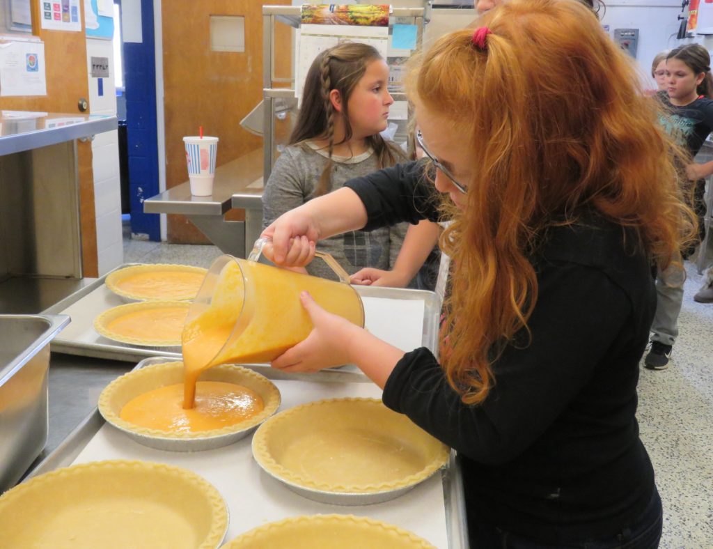 child pouring filling into pies