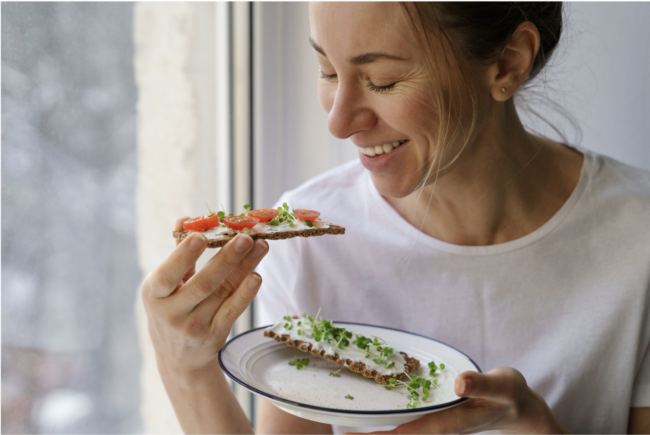 A woman eats whole grain crackers topped with a spread and fresh veggies