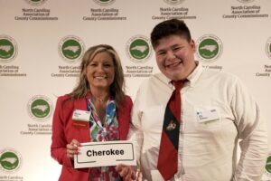 Two people stand together, one of them holds a piece of paper labeled Cherokee.